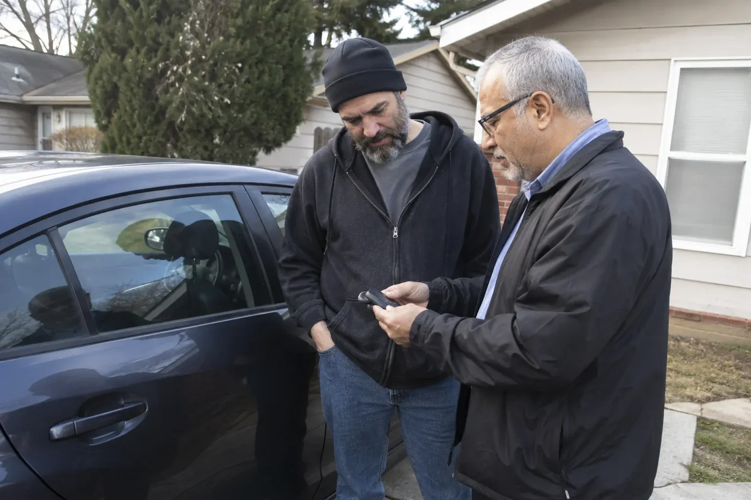 Two adults discussing a key fob beside a parked car. — Car Lockout Service, Ajax