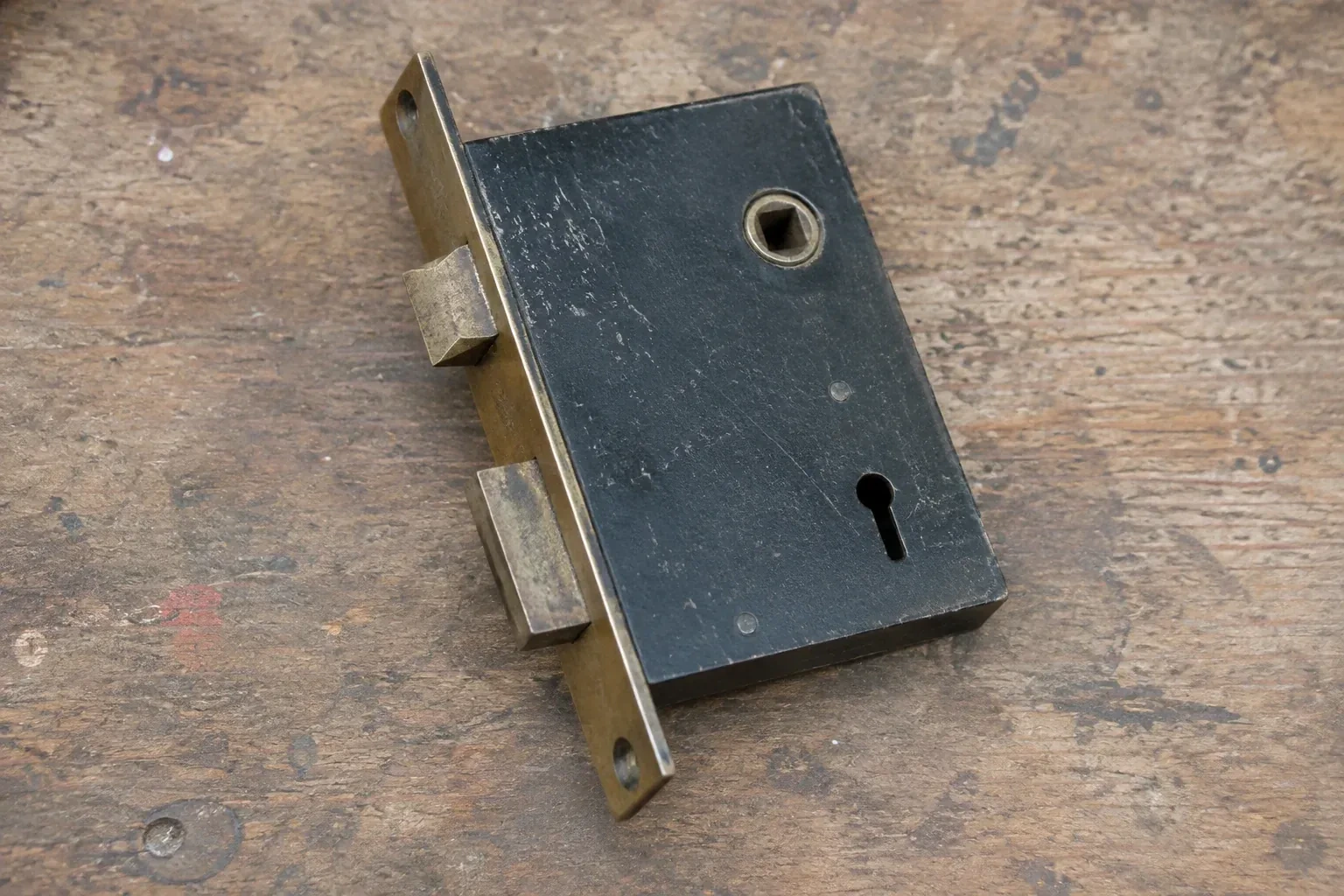 Closed mortise lock case with spindle opening, keyhole, latch and deadbolt on a wooden workbench. — Vintage Mortise Lock Service, Ajax